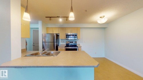 Open-concept kitchen featuring a double basin stainless steel sink, light wood cabinetry, and stainless steel appliances - 209 13908 136, Edmonton, AB 