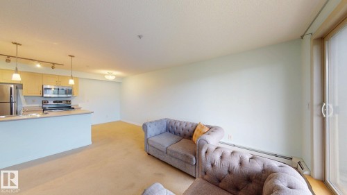 Open-concept living area featuring light wood-finish cabinetry, stainless steel appliances, a kitchen island with sink, and a glass sliding door - 209 13908 136, Edmonton, AB 