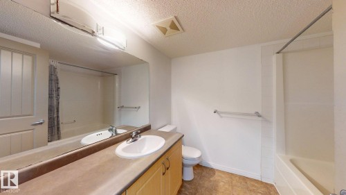 Full bathroom featuring a single vanity with an integrated sink, laminate countertop, and wood-finish cabinetry - 209 13908 136, Edmonton, AB 
