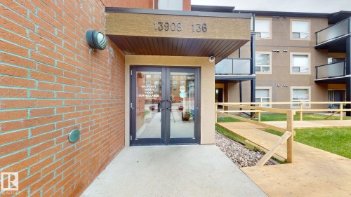 Brick exterior with dual glass entrance doors, featuring an overhead awning with address numerals - 209 13908 136, Edmonton, AB 