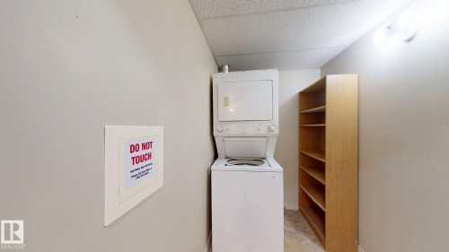 Dedicated laundry area featuring a stacked washer and dryer unit, ample built-in shelving, and overhead lighting - 209 13908 136, Edmonton, AB 