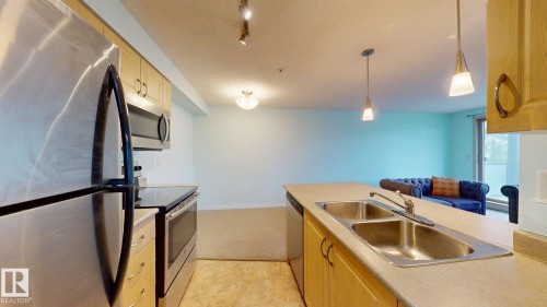 Kitchen featuring stainless steel appliances, light wood cabinetry, and a double basin sink - 209 13908 136, Edmonton, AB 