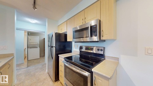 Kitchen area featuring light wood-finish cabinetry, stainless steel appliances including an oven with cooktop and an over-the-range microwave, and a side-by-side refrigerator - 209 13908 136, Edmonton, AB 