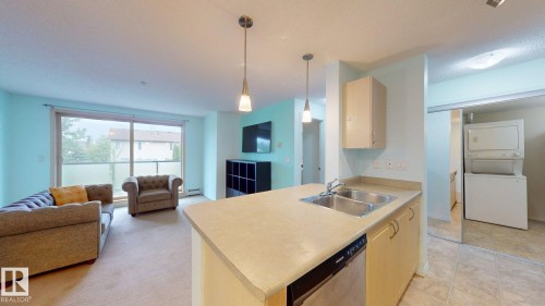 Open-concept living space featuring a kitchen island with dual sinks, light-toned cabinetry, and a built-in dishwasher - 209 13908 136, Edmonton, AB 