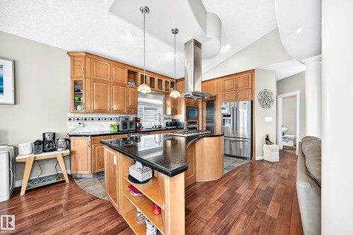 Kitchen featuring hardwood flooring, natural wood cabinetry, dark countertops, stainless steel appliances, and a central island with pendant lighting - 352 Ozerna Road, Edmonton, AB 