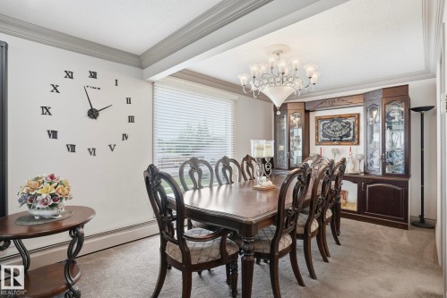 Formal dining space featuring a large chandelier, built-in display cabinetry, a rectangular window with horizontal blinds, and crown molding - 12131 101 Street Nw, Edmonton, AB 