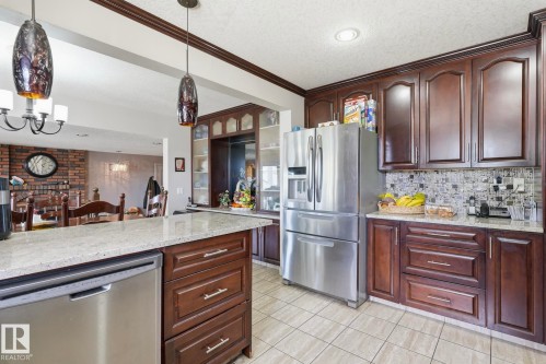 Kitchen featuring rich wood cabinetry with crown molding, stainless steel appliances, granite-look countertops, and a mosaic tile backsplash - 12131 101 Street Nw, Edmonton, AB 