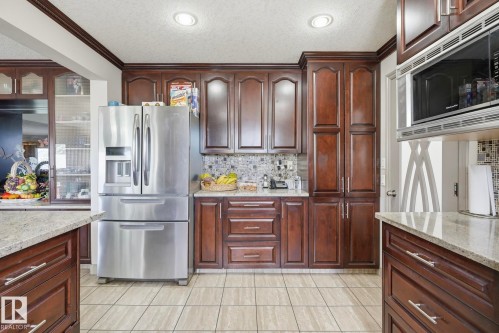 Kitchen featuring rich wood cabinetry, light-toned granite countertops, and stainless steel appliances - 12131 101 Street Nw, Edmonton, AB 