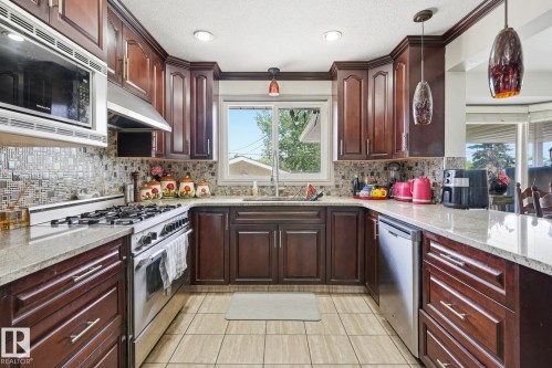 U-shaped kitchen featuring wood cabinetry, light-toned granite countertops, and a mosaic tile backsplash - 12131 101 Street Nw, Edmonton, AB 