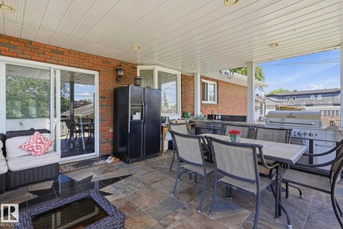 Covered patio featuring brick exterior, slate tile flooring, recessed lighting, and an outdoor kitchen area with a built-in grill - 12131 101 Street Nw, Edmonton, AB 