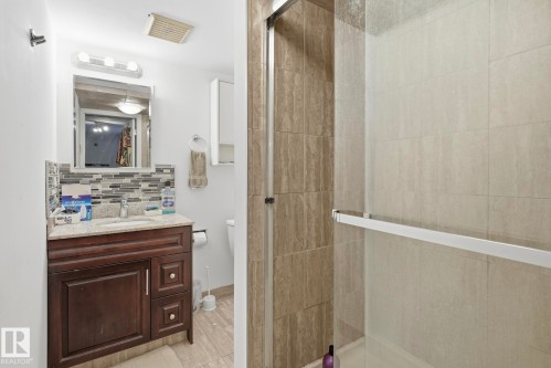 Bathroom featuring a dark wood-finish vanity with a light-colored countertop, an undermount sink, and a multi-toned mosaic tile backsplash - 12131 101 Street Nw, Edmonton, AB 