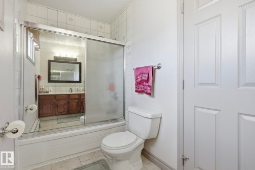 Bathroom featuring a tub with a sliding glass enclosure, white tiled walls with a diamond pattern, and a vanity with wood-finish cabinetry - 12131 101 Street Nw, Edmonton, AB 