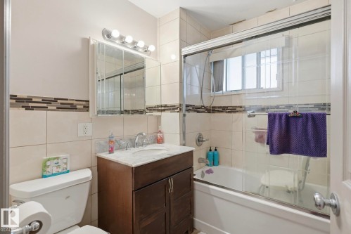 Tiled bathroom featuring a combination tub and shower with glass enclosure, a window, and a vanity with a white countertop - 12131 101 Street Nw, Edmonton, AB 