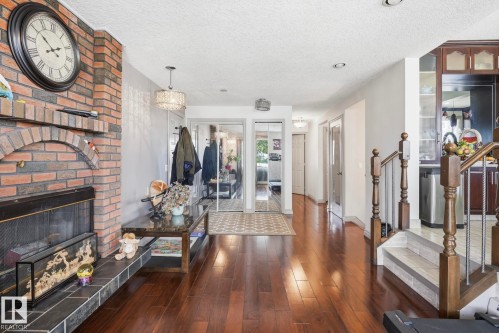 Brick fireplace with tile hearth, wood-finish flooring, mirrored closet doors, and hardwood staircase - 12131 101 Street Nw, Edmonton, AB 