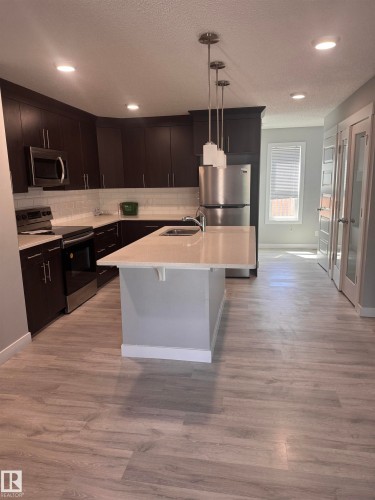 Kitchen featuring dark wood cabinetry, stainless steel appliances, light-toned countertops, a subway tile backsplash, and light wood-finish flooring - 1313 Chappelle Boulevard, Edmonton, AB 