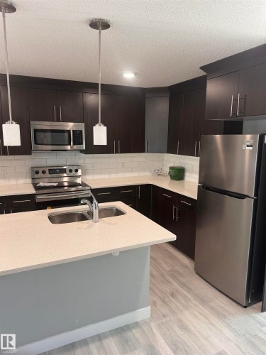 Contemporary kitchen featuring dark wood-finish cabinetry, stainless steel appliances, light-toned countertops, and a subway tile backsplash - 1313 Chappelle Boulevard, Edmonton, AB 