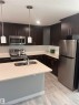 Contemporary kitchen featuring dark wood-finish cabinetry, stainless steel appliances, light-toned countertops, and a subway tile backsplash - 1313 Chappelle Boulevard, Edmonton, AB 