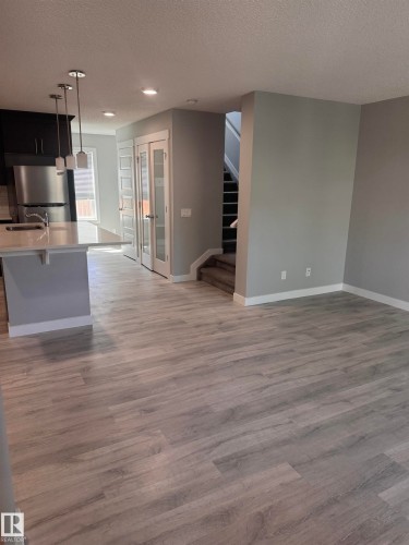 Open-concept living area featuring light wood-finish flooring, a contemporary kitchen island with pendant lighting, stainless steel appliances, and French doors - 1313 Chappelle Boulevard, Edmonton, AB 