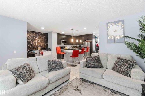 Open-concept living space featuring light-toned flooring, recessed lighting, a kitchen island with pendant lighting, dark wood-finish cabinetry, and stainless steel appliances - 1313 Chappelle Boulevard, Edmonton, AB 