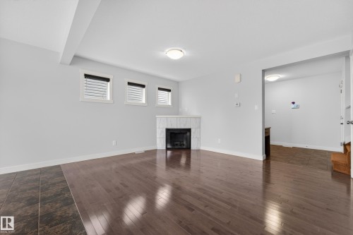 Living area featuring wood-finish flooring, a corner fireplace with a tiled surround, and three windows with blinds - 5244 1A Avenue, Edmonton, AB 