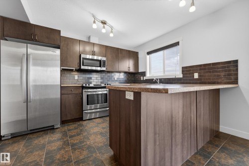 Kitchen featuring stainless steel appliances, dark wood-finish cabinetry, a subway tile backsplash, an island with countertop seating, and patterned floor tiling - 5244 1A Avenue, Edmonton, AB 