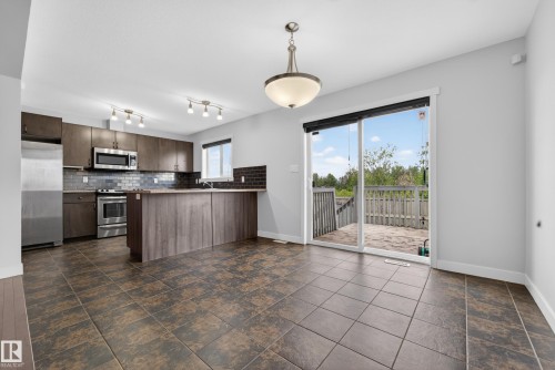 Spacious kitchen and dining area featuring durable tile flooring, stainless steel appliances, dark wood-finish cabinetry, and a sliding glass door leading to a private outdoor deck - 5244 1A Avenue, Edmonton, AB 