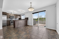 Spacious kitchen and dining area featuring durable tile flooring, stainless steel appliances, dark wood-finish cabinetry, and a sliding glass door leading to a private outdoor deck - 