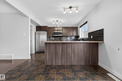 Kitchen featuring wood-finish cabinetry, stainless steel appliances, a dark subway tile backsplash, and a breakfast bar with a speckled countertop - 5244 1A Avenue, Edmonton, AB 