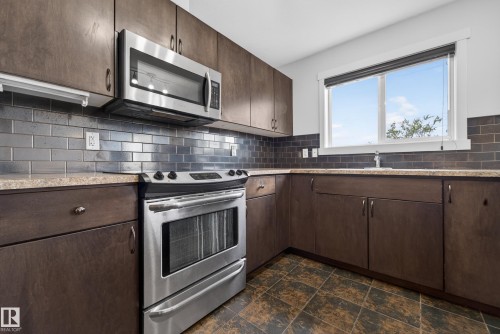Modern kitchen featuring stainless steel appliances, dark wood-finish cabinetry, and a subway tile backsplash - 5244 1A Avenue, Edmonton, AB 