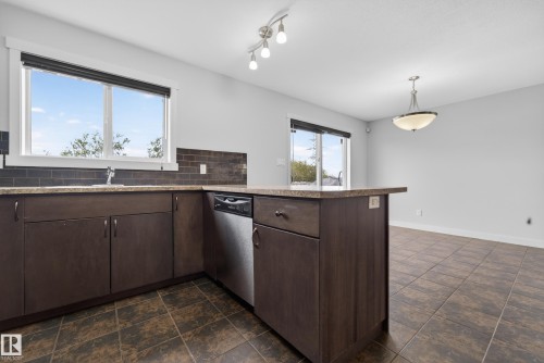 Kitchen featuring dark wood-finish cabinetry, a stainless steel dishwasher, and a breakfast bar - 5244 1A Avenue, Edmonton, AB 