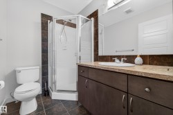 Enclosed glass shower stall complemented by a dark wood-finish vanity with an integrated sink and chrome fixtures - 