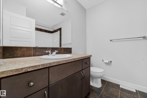 Bathroom featuring a dark wood-finish vanity with a light-toned countertop, an integrated sink, and a tiled backsplash - 5244 1A Avenue, Edmonton, AB 
