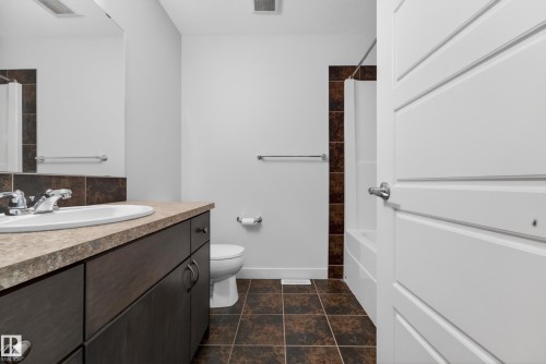 Bathroom featuring a spacious vanity with an integrated sink, dark wood-finish cabinetry, and a stone-look countertop - 5244 1A Avenue, Edmonton, AB 