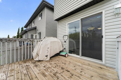 Outdoor wood deck with a sliding glass patio door, white vinyl siding, and an exterior wall lantern - 5244 1A Avenue, Edmonton, AB 