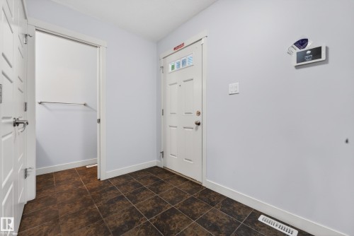 Entryway featuring a white paneled door, square brown floor tiling, and a recessed alcove with a wall-mounted bar - 5244 1A Avenue, Edmonton, AB 