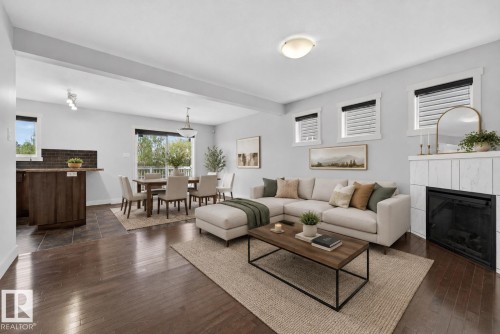 Open-concept living space featuring wood-finish flooring, a contemporary fireplace with a white tile surround, and multiple windows - 5244 1A Avenue, Edmonton, AB 
