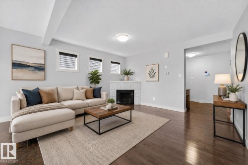 Spacious living area featuring rich wood-finish flooring, a tiled fireplace with a white mantel, and recessed lighting - 5244 1A Avenue, Edmonton, AB 