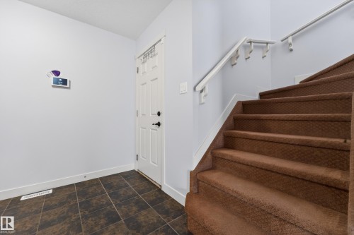 Entryway featuring a paneled door with black hardware, brown tile flooring, and a carpeted staircase with white handrails - 5244 1A Avenue, Edmonton, AB 