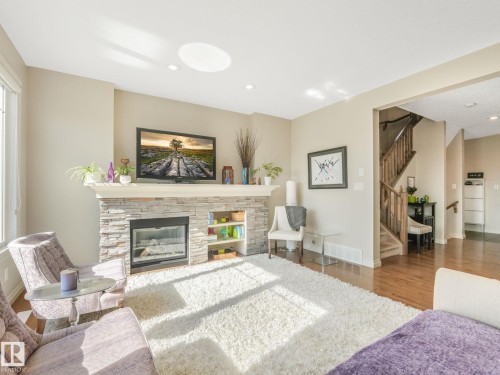 Living room featuring a stacked stone fireplace with a white mantel and built-in shelving - 3 1641 James Mowatt Trail, Edmonton, AB 