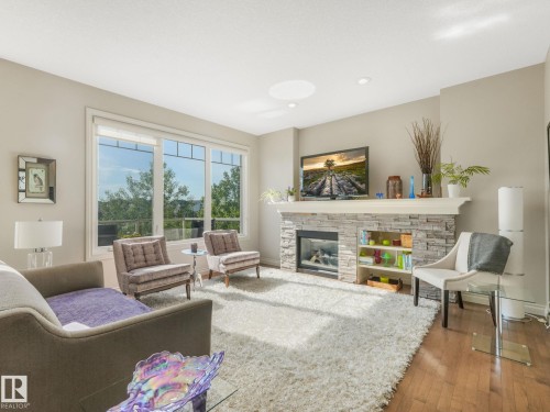Spacious living area featuring a stone-clad fireplace with built-in shelving, large windows, recessed lighting, and wood-finish flooring - 3 1641 James Mowatt Trail, Edmonton, AB 