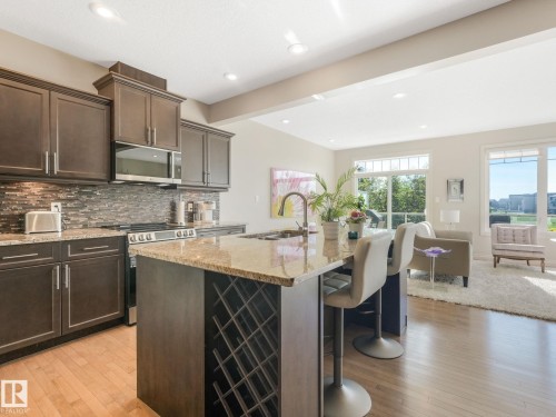 Kitchen featuring dark wood cabinetry, granite countertops, and a full tile backsplash - 3 1641 James Mowatt Trail, Edmonton, AB 