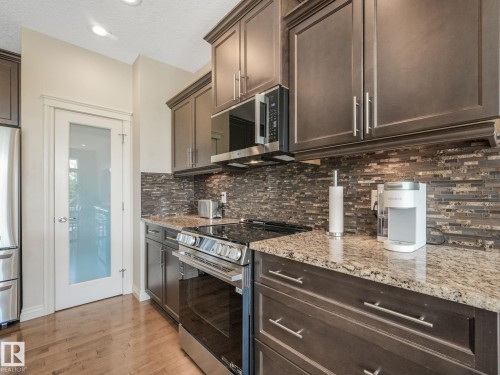 Kitchen featuring wood-finish flooring, granite countertops, an undermount sink, and dark wood cabinetry - 3 1641 James Mowatt Trail, Edmonton, AB 