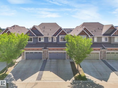 Townhouse exteriors featuring stone accents, gabled roofs, attached garages, paved driveways, and mature trees - 3 1641 James Mowatt Trail, Edmonton, AB 