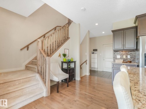 Staircase featuring light wood newel posts and spindles, carpeted treads, and a wood handrail - 3 1641 James Mowatt Trail, Edmonton, AB 