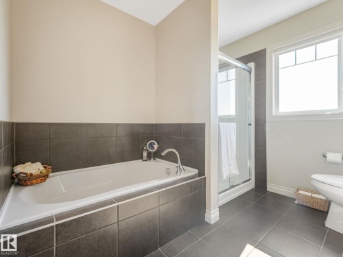 Bathroom featuring a built-in tub with tile surround, a separate glass-enclosed shower, a large window, and tile flooring - 3 1641 James Mowatt Trail, Edmonton, AB 