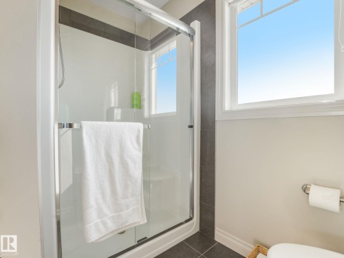 Shower enclosure with sliding glass doors, dark tile surround, and a built-in shower bench - 3 1641 James Mowatt Trail, Edmonton, AB 