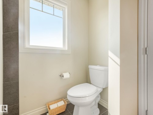 White toilet with a round bowl and tank, set against a light beige wall - 3 1641 James Mowatt Trail, Edmonton, AB 