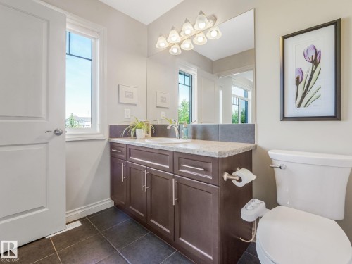 Vanity featuring a single undermount sink, stone countertop, and dark wood-finish cabinetry - 3 1641 James Mowatt Trail, Edmonton, AB 