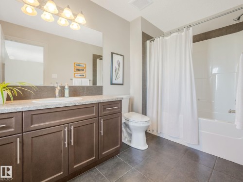 Bathroom featuring a dark wood vanity with a light-toned countertop, a large wall-mounted mirror, a tub/shower combination, and dark grey tile flooring - 3 1641 James Mowatt Trail, Edmonton, AB 