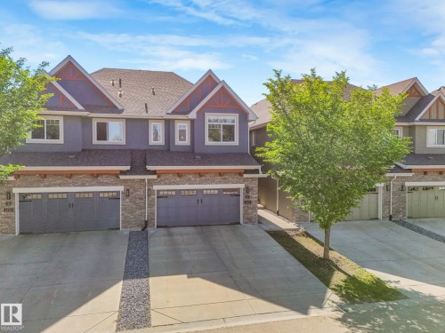Contemporary townhome exterior featuring an attached garage, paved driveway, stone accents, and a shingled roof - 3 1641 James Mowatt Trail, Edmonton, AB 